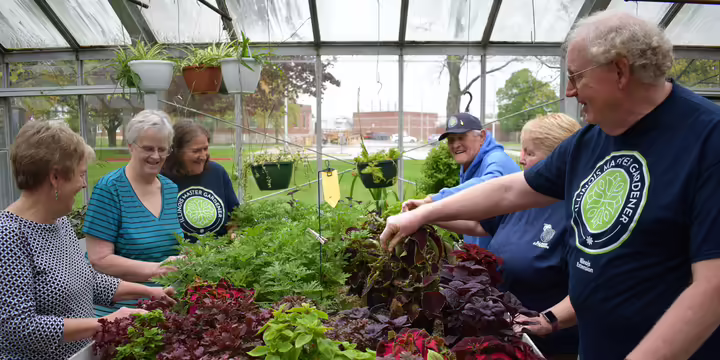 A group of Master Gardeners smiling and convening in a greenhouse.