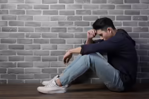 Hombre sentado frente una pared de ladrillo deteniendose la frente con la mano