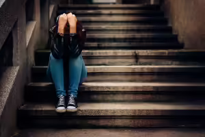 Lone person sitting on deserted steps with elbows on knees and hands covering face