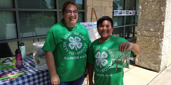 adult lady and youth in 4-H shirts holding pencils in water