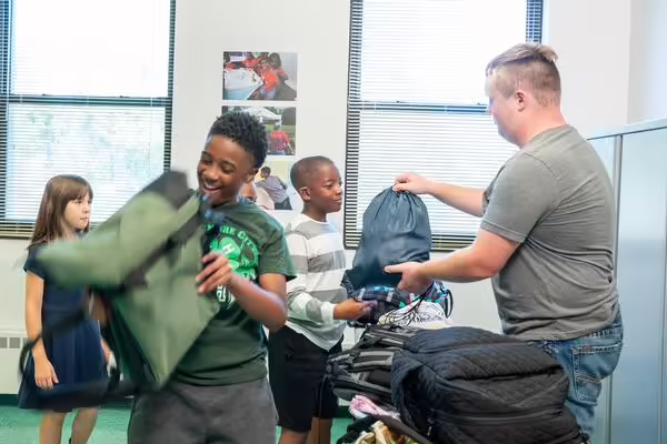 excited students receive backpack and supplies from older 4-H member