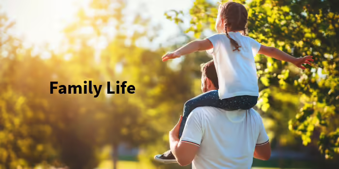 A little girl with arms outstretched is sitting on her father's shoulders.