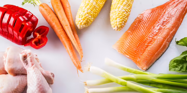 raw vegetables and raw meat being cut on a cutting board