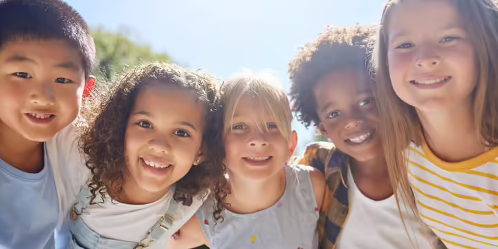 Five children smiling gathered with arms around each other.