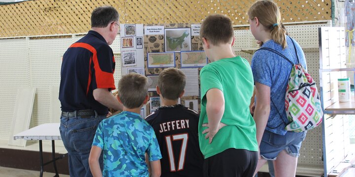 Adults and youth standing at a table looking at a display board.
