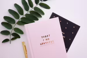 Pen and gratitude journal titled "Today I Am Grateful" lying next to a plant leaf