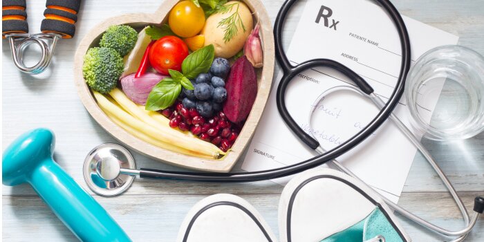 healthy fruit, gym weights, stethoscope and water presented on table
