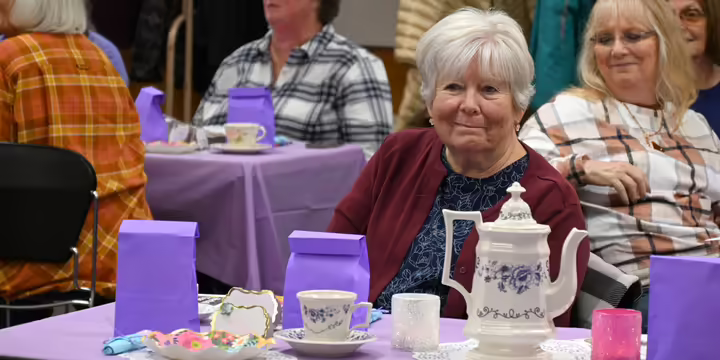Woman smiling while sitting at a table with a tea pot