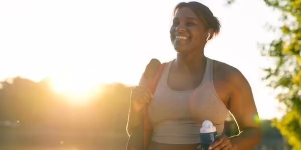 A woman taking a walk and smiling as the sun shines behind her.