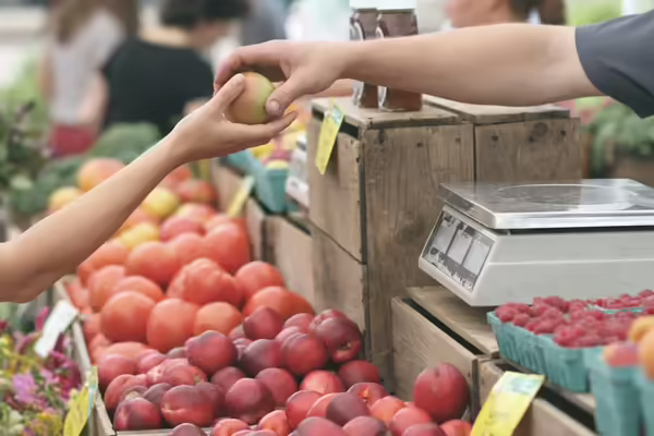 Arm reaching out to give another person a peach in a market stall.