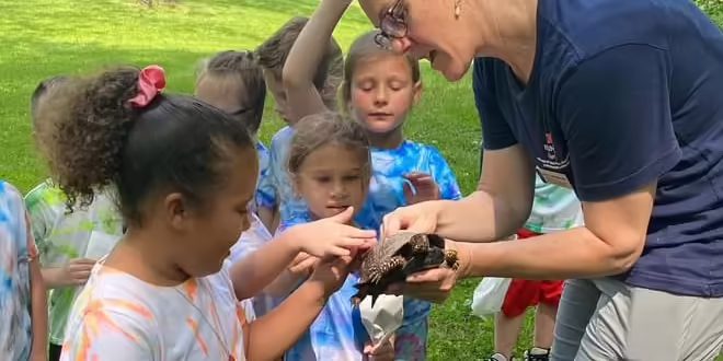a woman holds a turtle for a child to touch