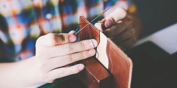 A person sewing a leather wallet. 