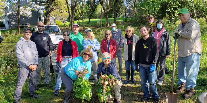 a group of volunteers stand holding invasive plants they pulled