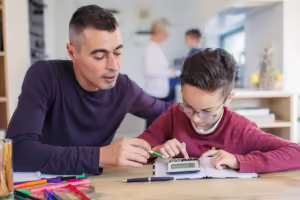 Man helping grade school aged boy use calculator for homework