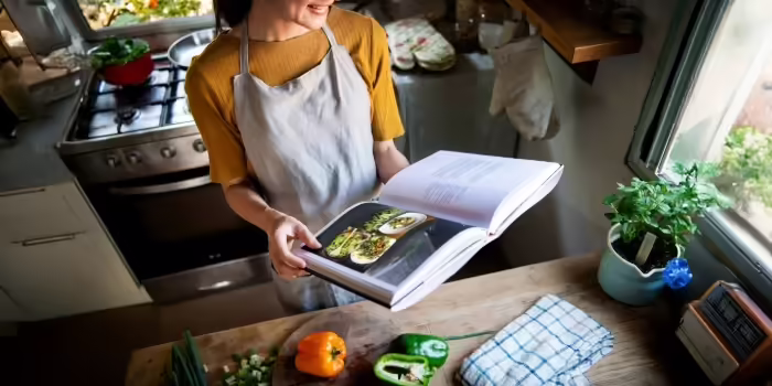 A woman holding a recipe book at her kitchen counter 