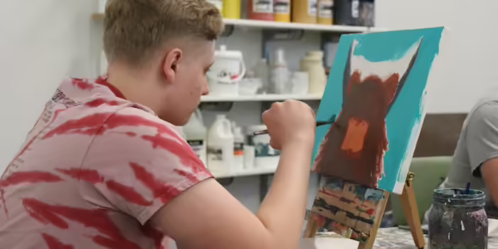 A teen boy painting a canvas of a highland cow.