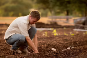 Farmer kneeling with hands in the dirt 