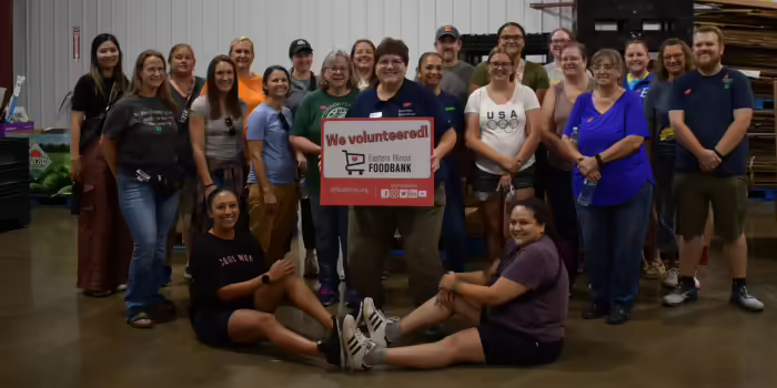 A group of people posing for a picture. One person is holding a sign that says, "We volunteered!"