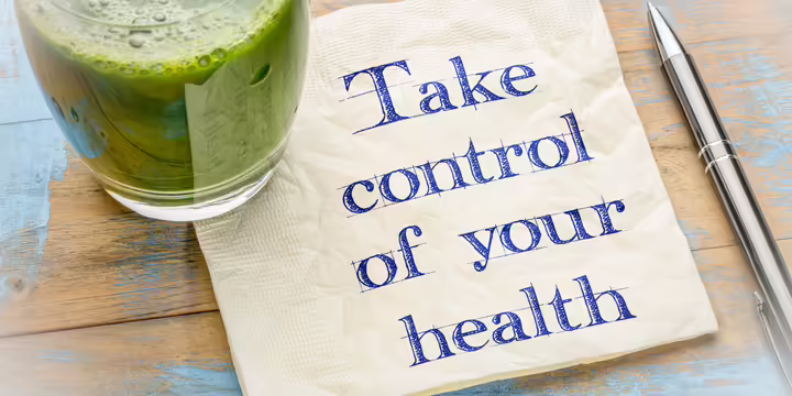 A napkin with the words, "Take control of your health" written on it along side of a glass filled with a green smoothie.
