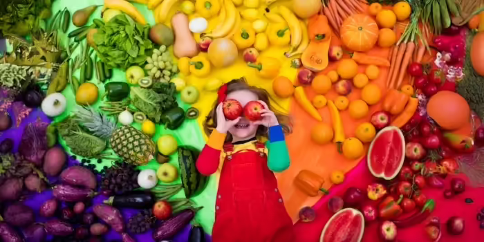 A small child surrounded by a variety of brightly colored fruits and vegetables 