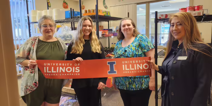 Four people hold up a ribbon inside a food pantry room