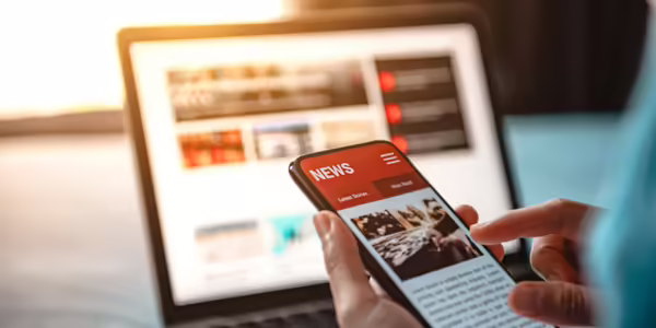 News on a mobile phone with laptop in the background