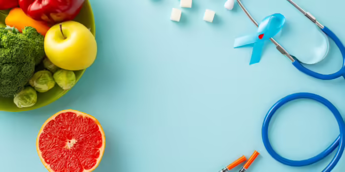 A bowl of fruits and vegetables with a blue awareness ribbon, stethoscope, sugar cubes, and insulin syringe displayed nearby.