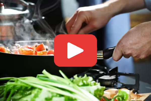 A person cooking food in a skillet with a YouTube play button graphic over the top of the image.