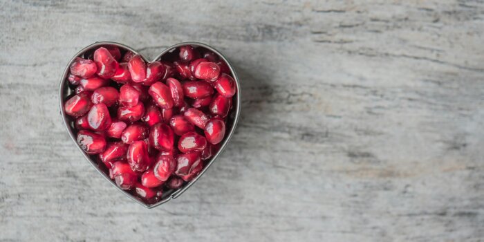 A heart shaped bowl of pomegranate seeds. 