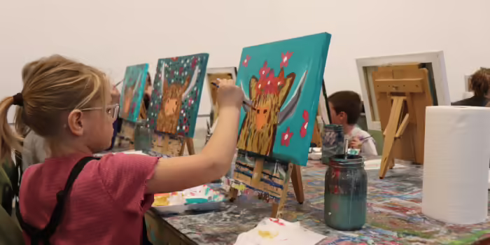 A young 4-H youth paints a picture of a highland cow.