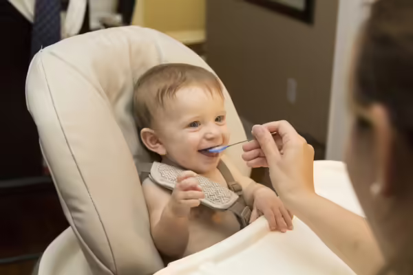 young child eating baby food in high chair.