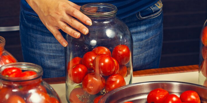 lady putting ripe, small tomatoes in glass jars during canning process