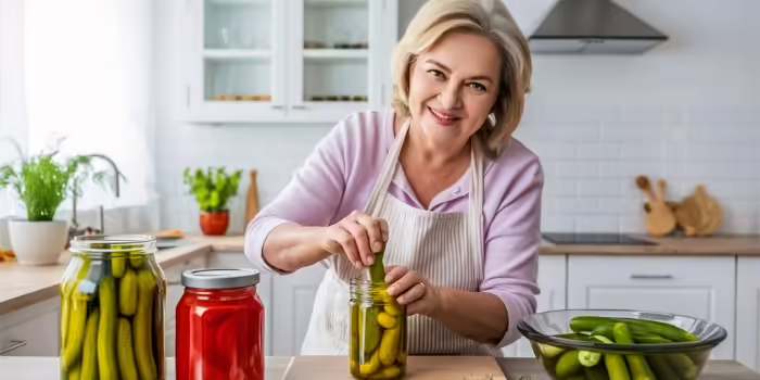 smiling woman putting pickles in canning jar
