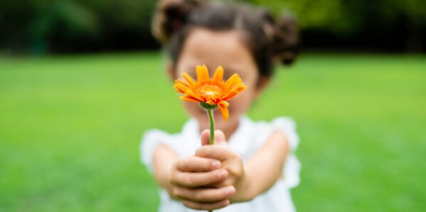 young child holding out a flower