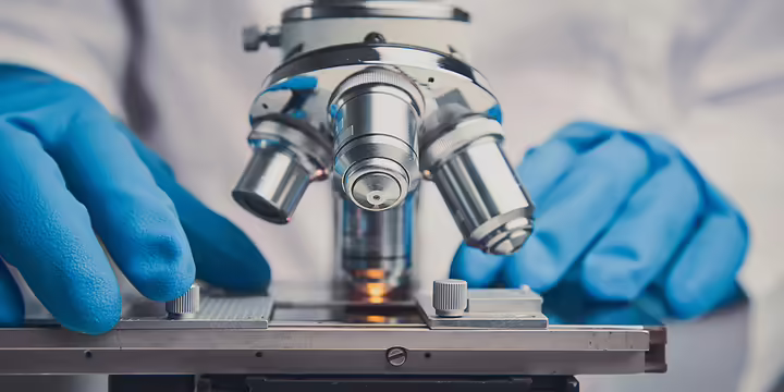 gloved hands on a microscope
