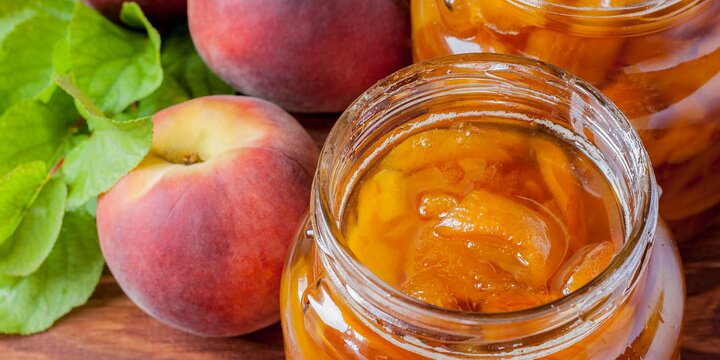 peach jam in jar in front of two fresh whole peaches