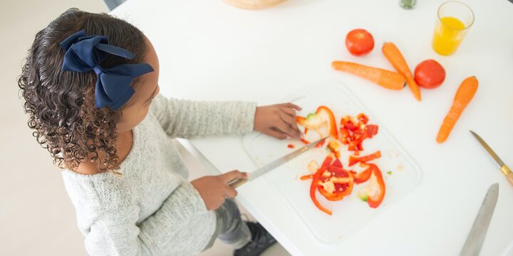 A young girl cutting vegetables on a cutting board.