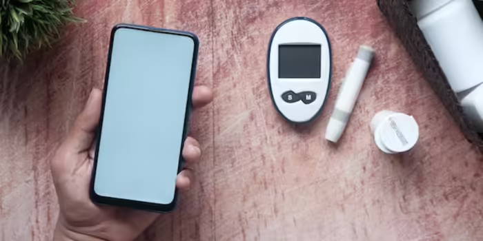 A person holding a smart phone in their left hand over a table with a glucose monitor and a pill bottle.