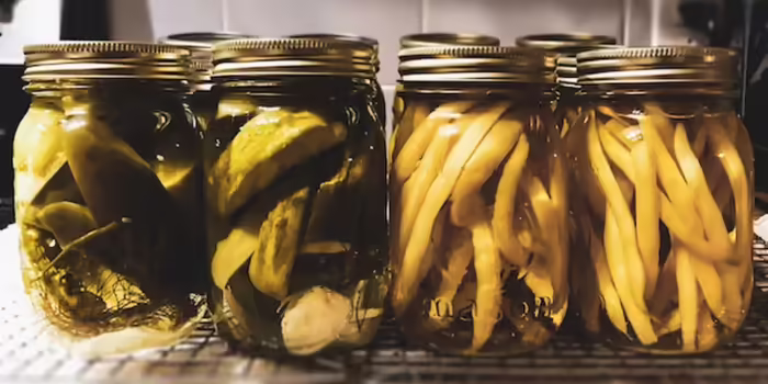Two jars of canned pickles and two jars of canned wax beans on countertop.