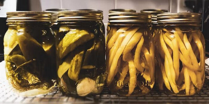 Two jars of canned pickles and two jars of canned wax beans on countertop.