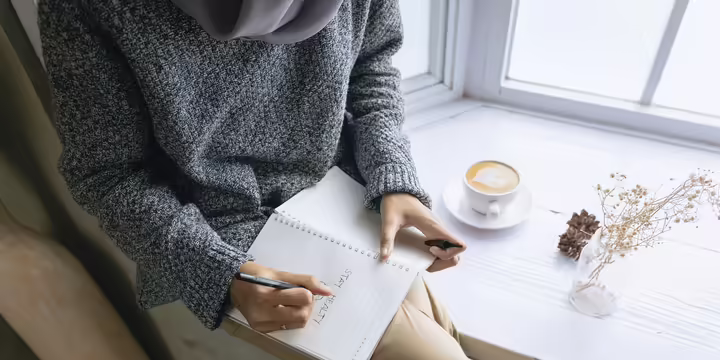 A person journals seated in a window