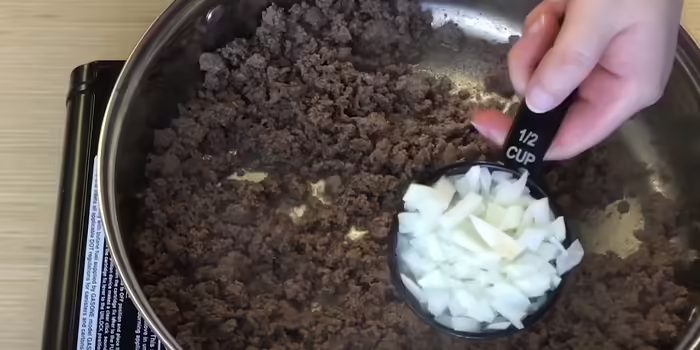 adding chopped onion to cooked, ground venison in a skillet