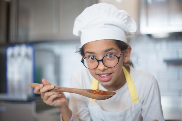 A girl wearing a chefs hat and holding a spoon 