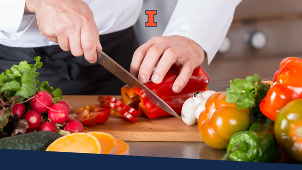 A chef chopping up a red pepper on a cutting board with a variety of vegetables surrounding the board.