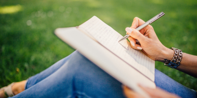 lady sitting in grass writing in notebook