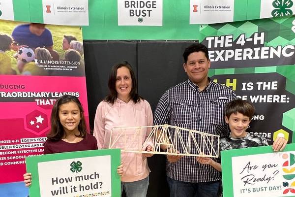 family holding a wooden bridge model with signs saying Bridge Bust