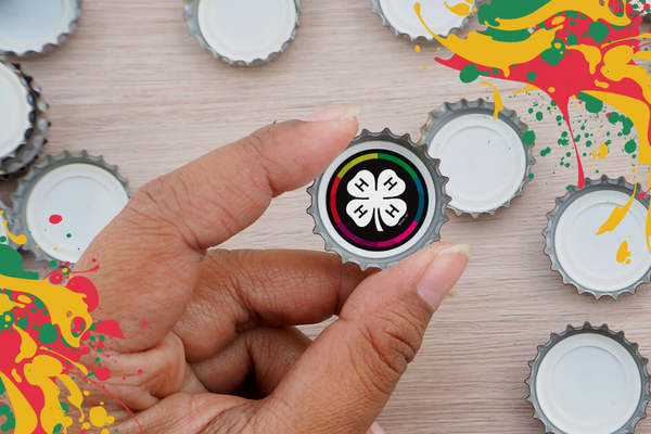 close up of hand holding bottle cap with 4-H emblem