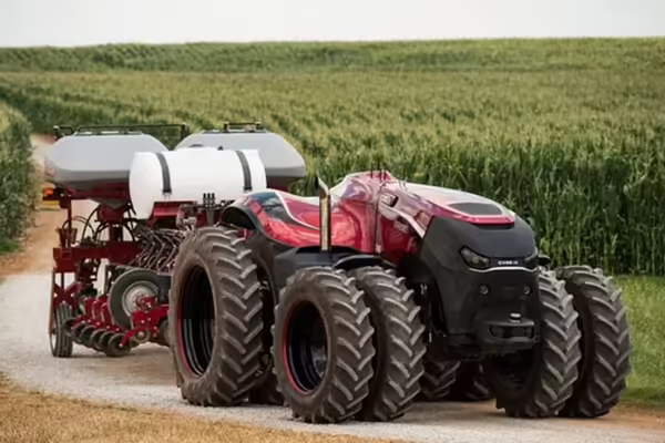 Red automated tractor driving through roadway near field.