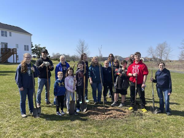 groups of people holding shovels and with a newly planted oak tree