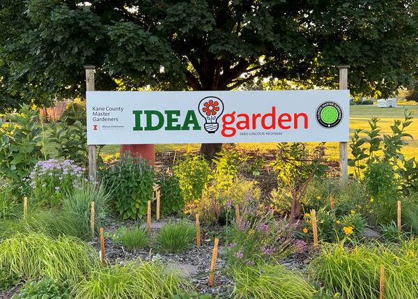 Idea Garden sign in orange and green with plants all around it